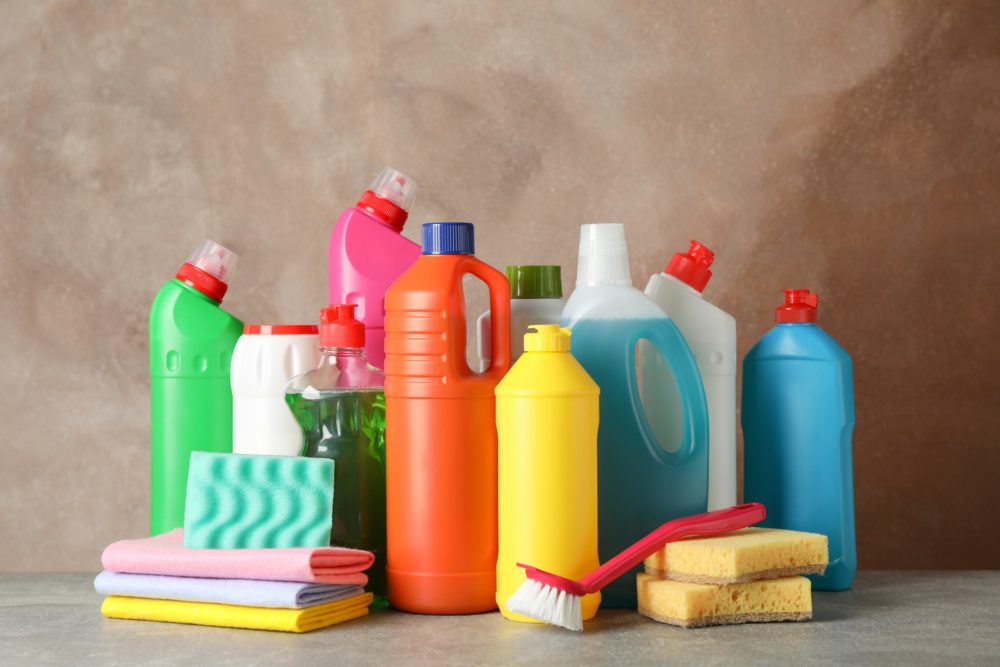 Bottles with detergent and cleaning supplies on brown background, space for text