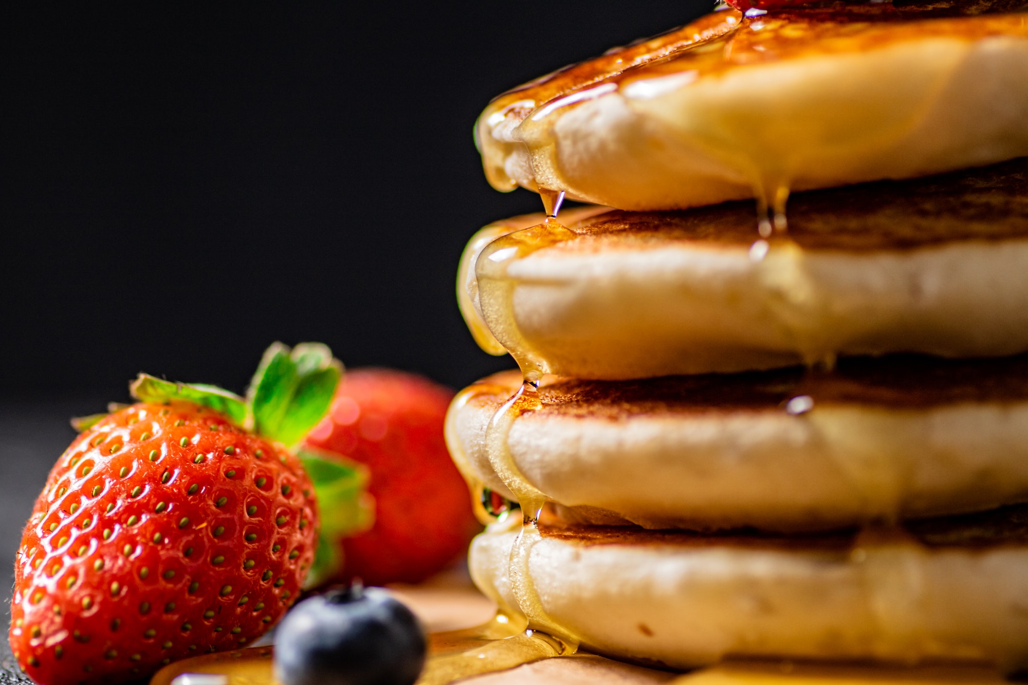 A pile of pancakes with berries and honey.