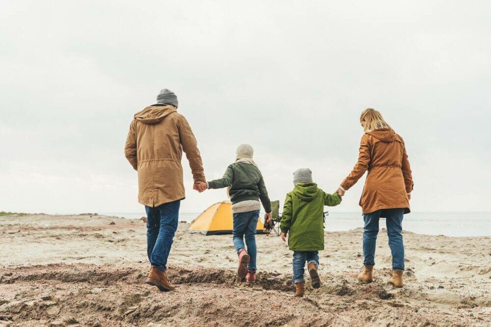 back view of family walking to camping tent on seashore on cloudy day