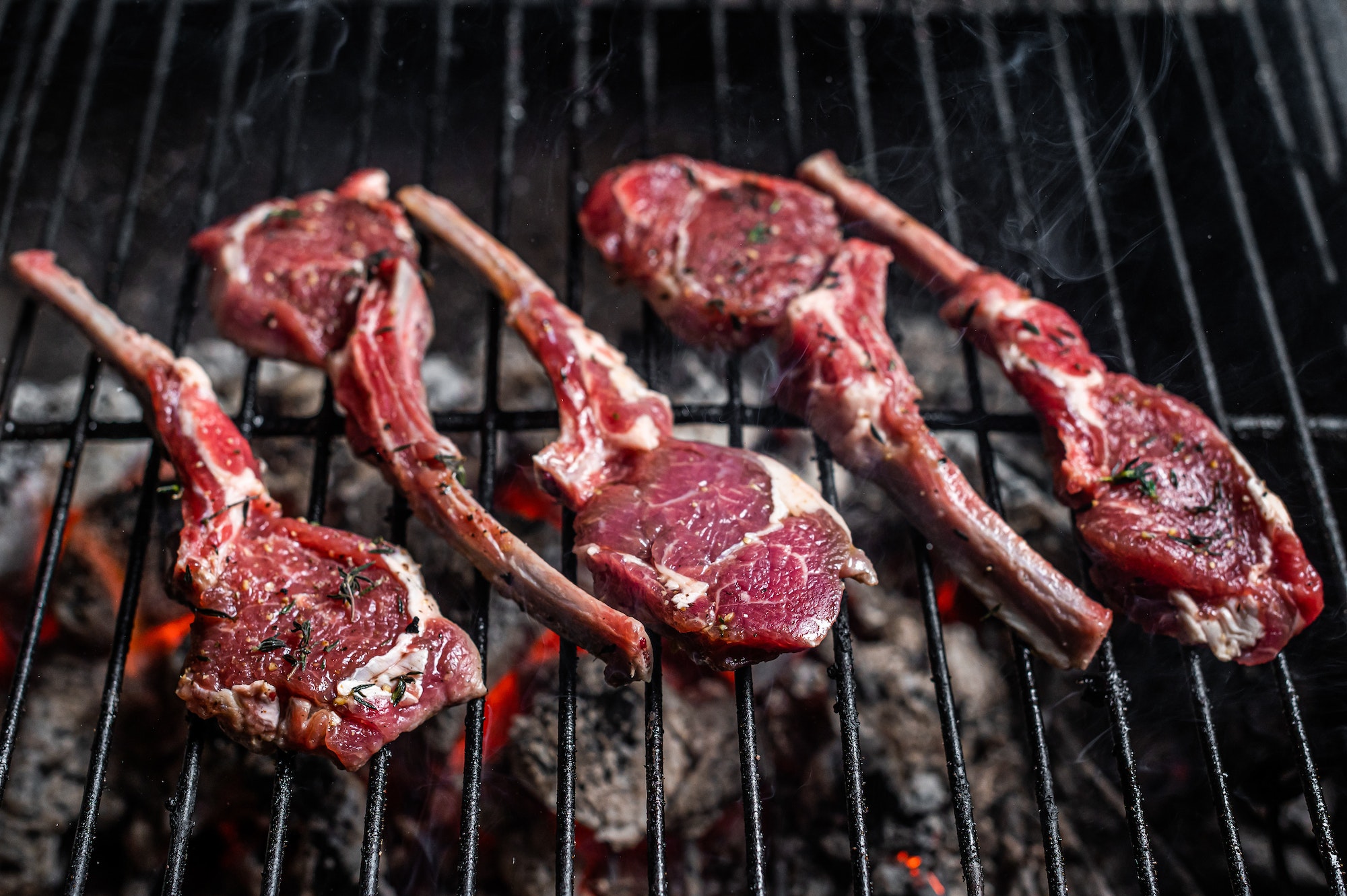 Cooking of raw lamb chop steaks on barbecue, outdoor BBQ grill with fire. Top view