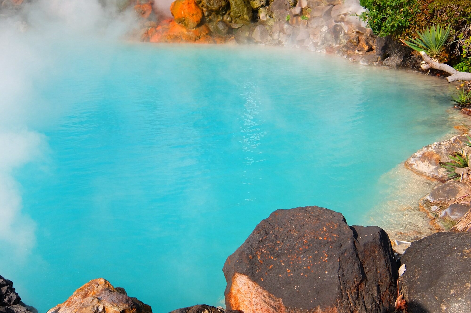 Lava rocks beside turquoise color hot spring
