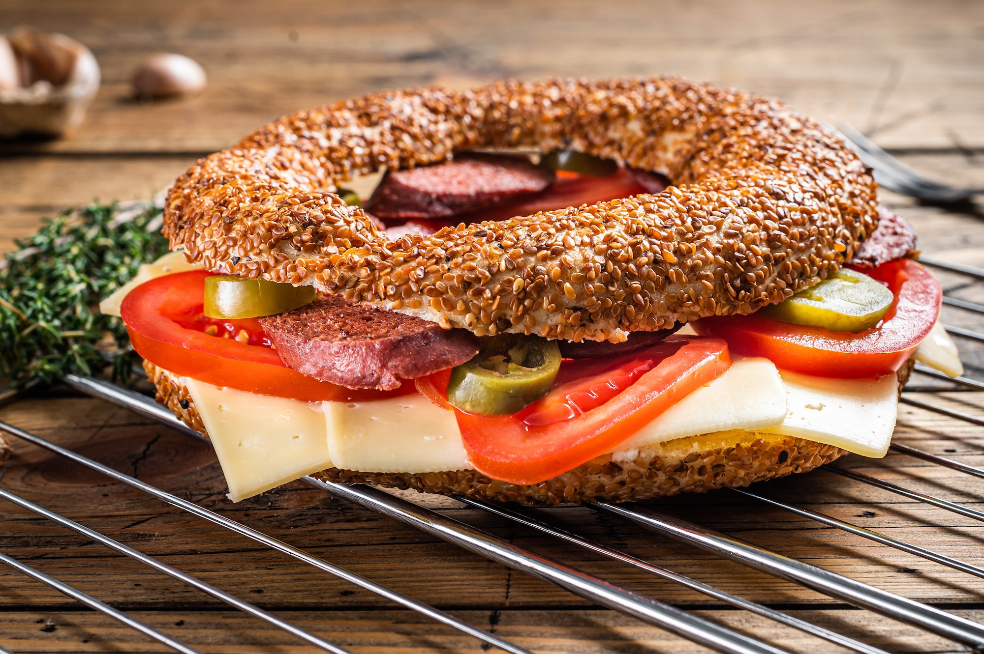 Bagel sandwich with lettuce, tomato, yellow cheese and sausages. Wooden background. Top view