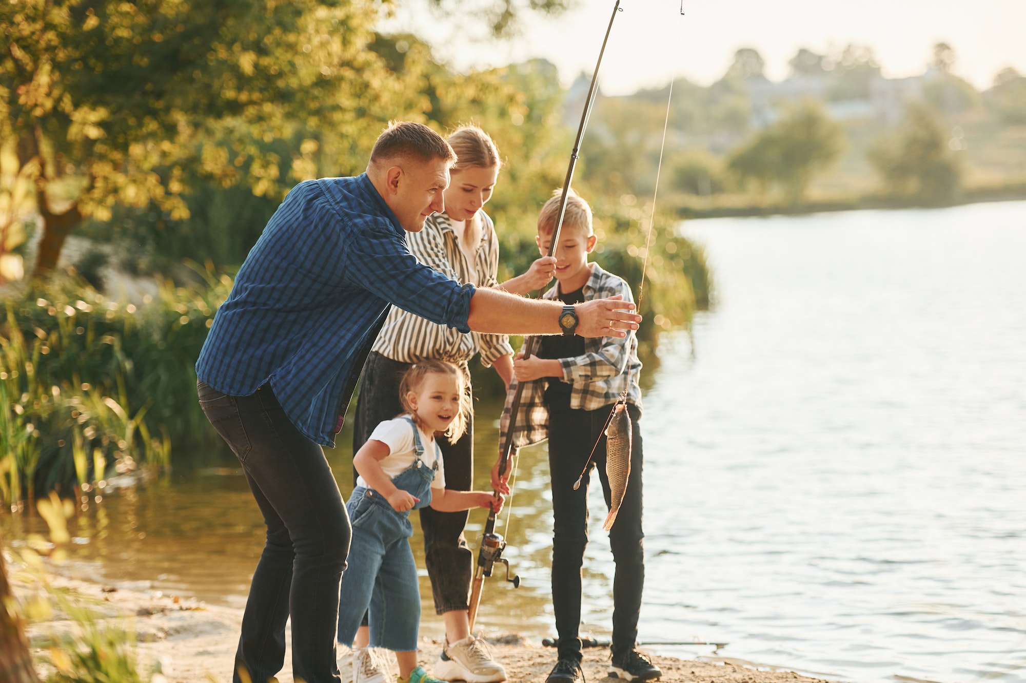 Father and mother with son and daughter on fishing together outdoors at summertime