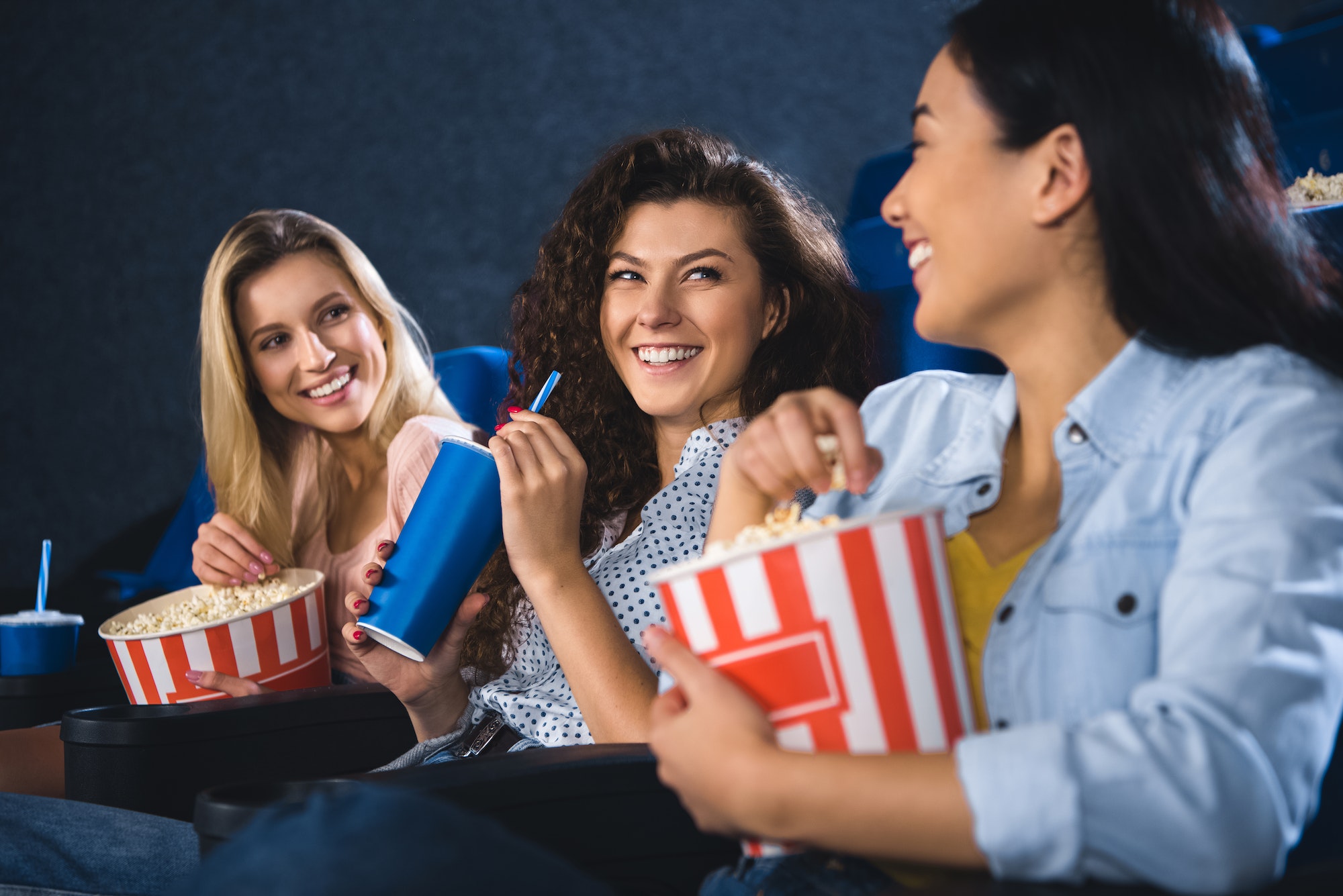 happy multiracial women with popcorn watching film together in movie theater
