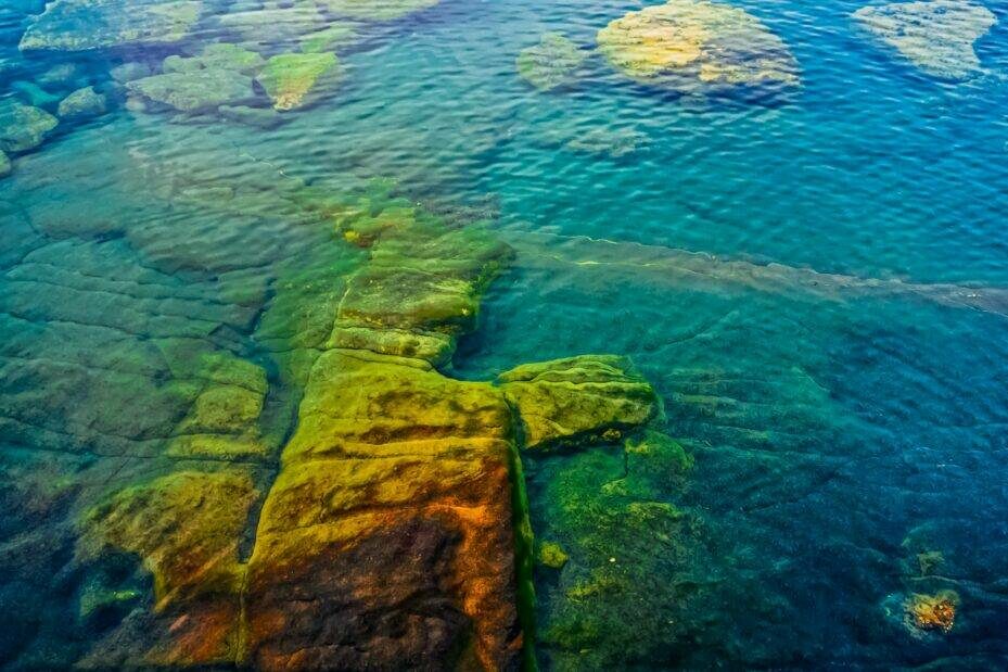 Turquoise blue green waters with algae covered rocks below the surface