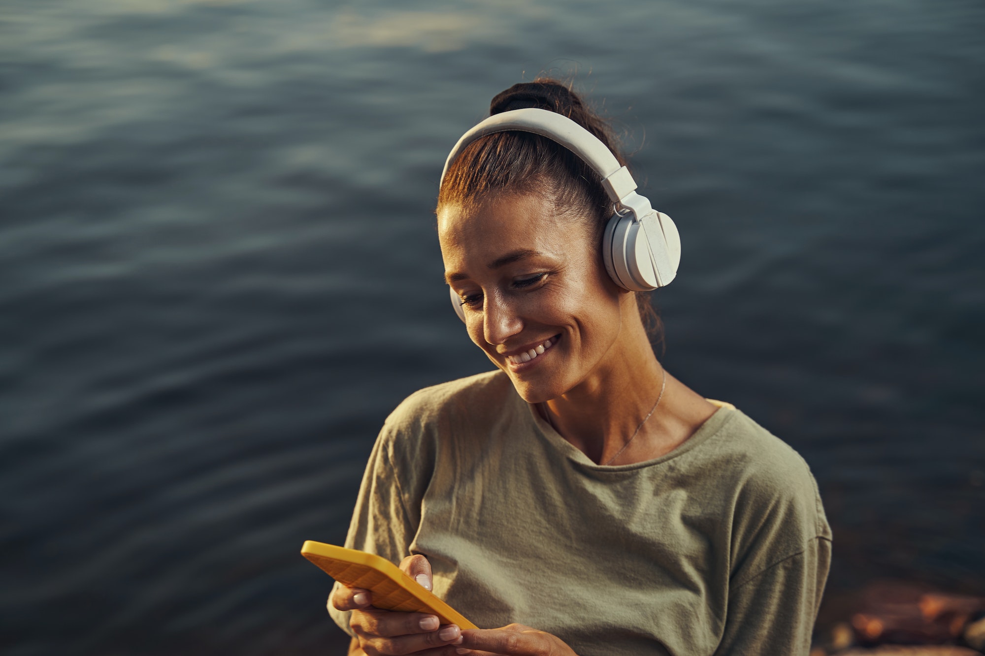 Woman listening to music in headphones near lake