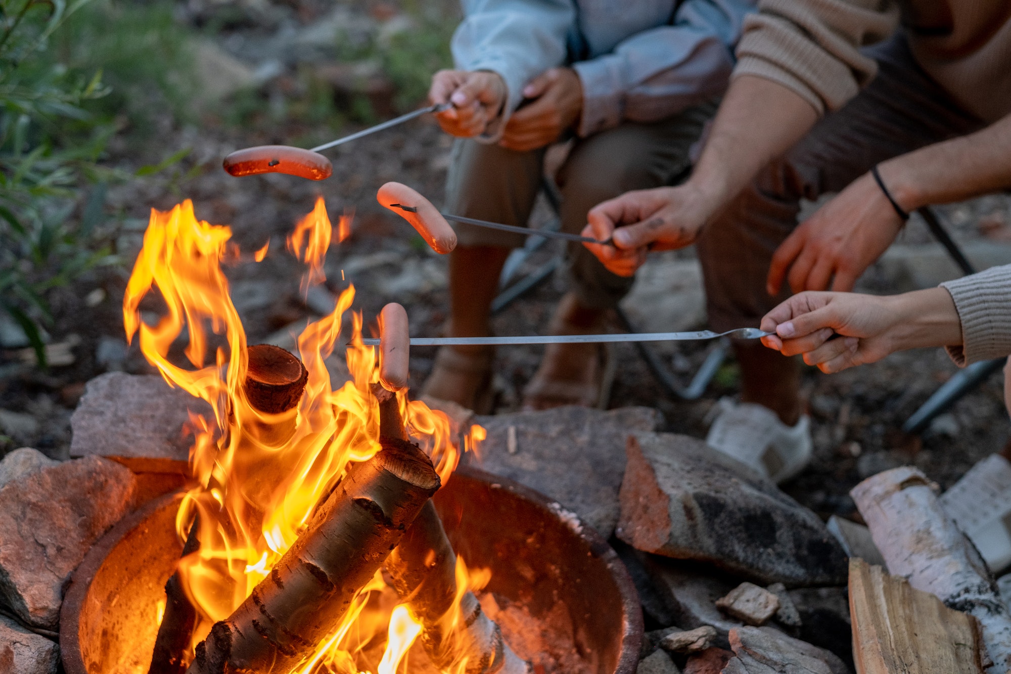 Young family of three cooking sausages over campfire