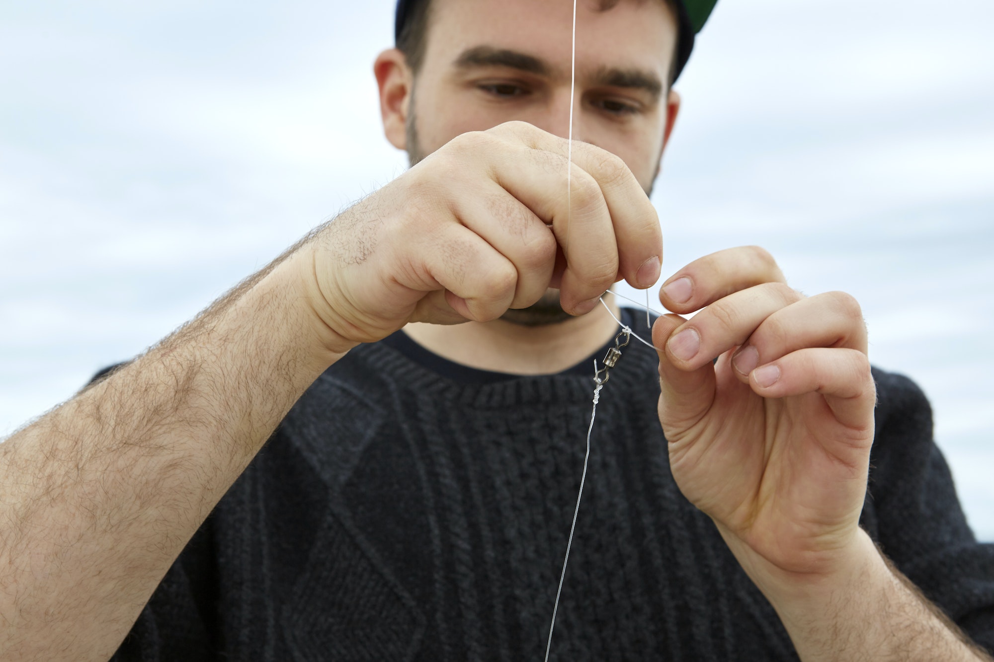 Young man attaching fishing hook to fishing line