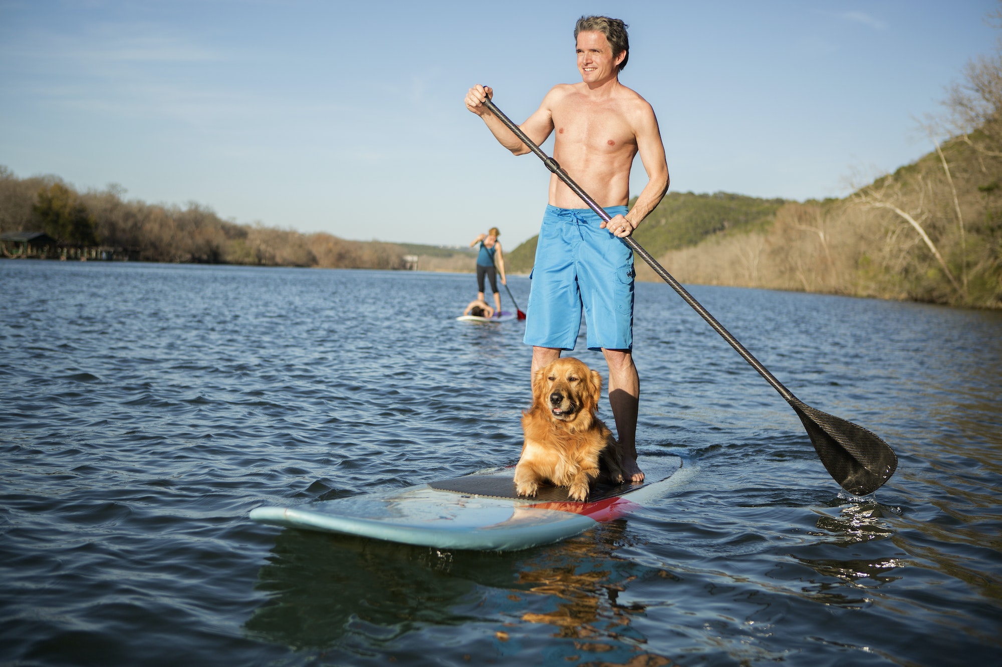 A man standing on a paddleboard with a dog.