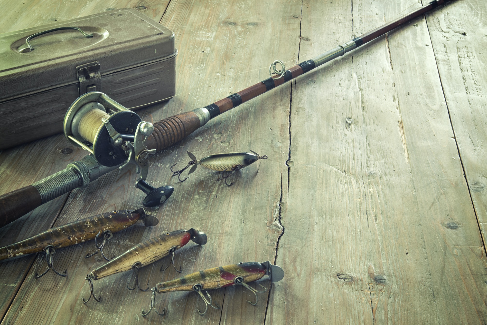 Antique Fishing Rod with Lures and Tackle Box on Wood Surface