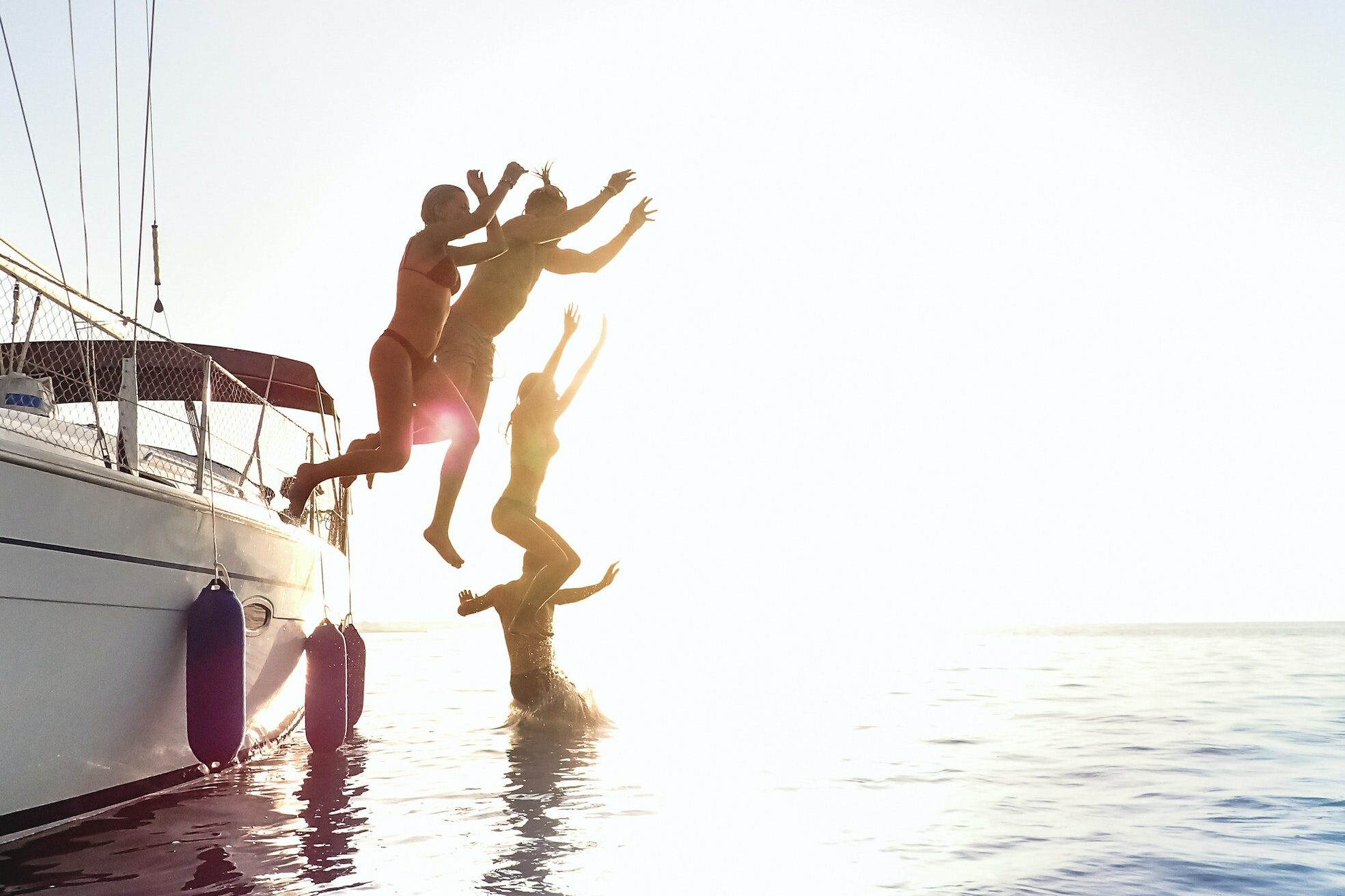Side view of young millennial friends jumping from sailboat on sea ocean trip