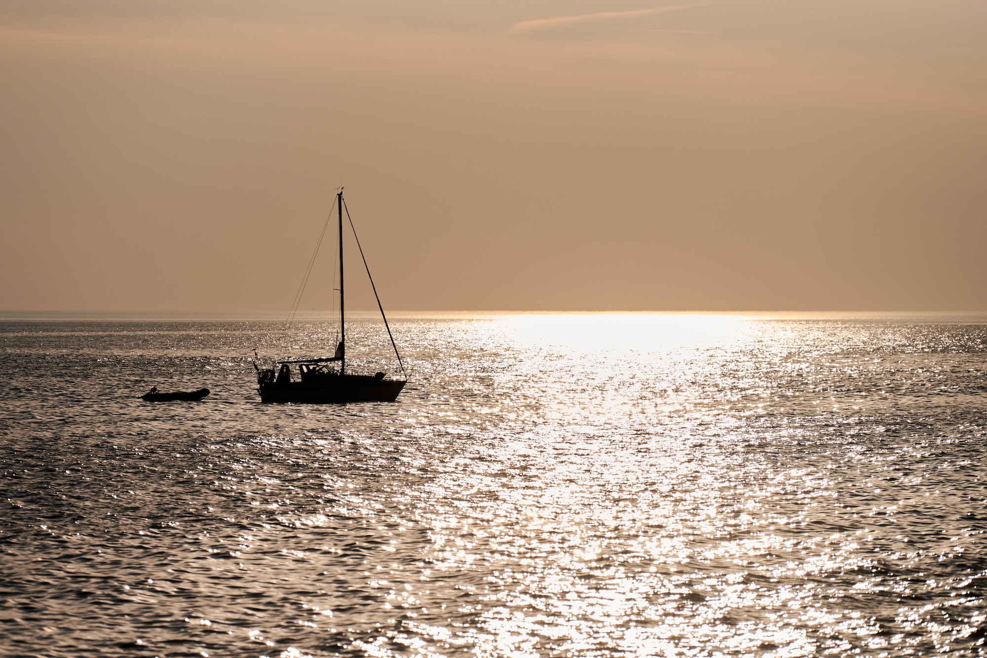 Two sailing boats silhouettes on background of beautiful sunset with reflection in calm seawater