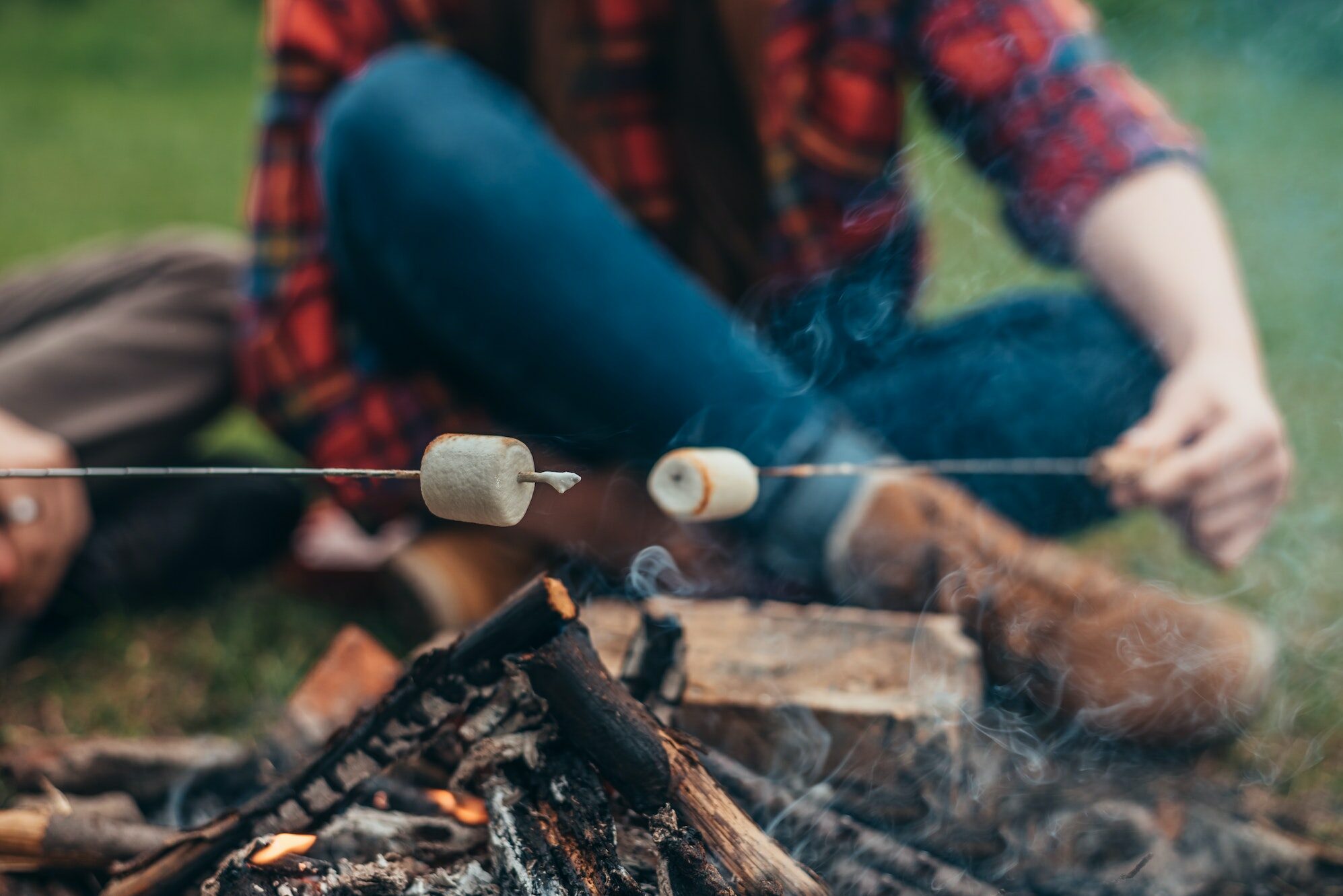 Woman in a blur while holding a marshmallow above the camping fire