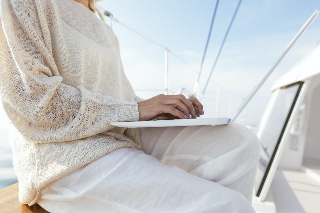 Woman sitting on catamaran, using laptop
