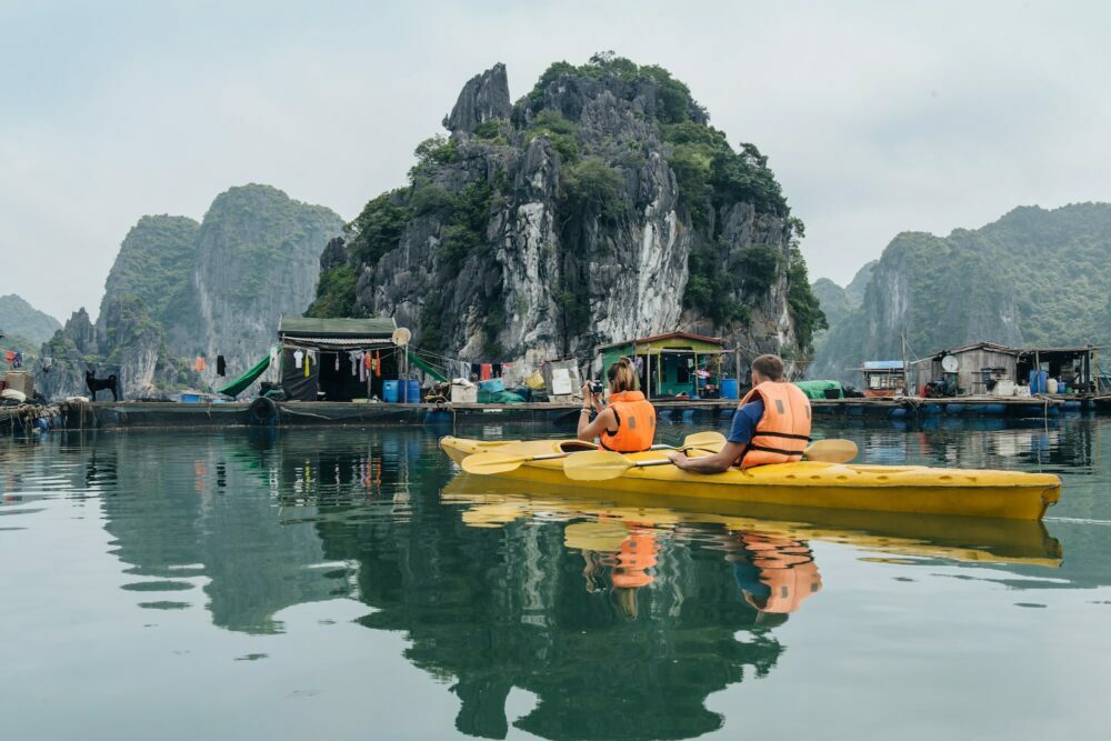 Couple exploring floating village on kayak and taking photograps in the boat. Ha Long Bay, Vietnam,