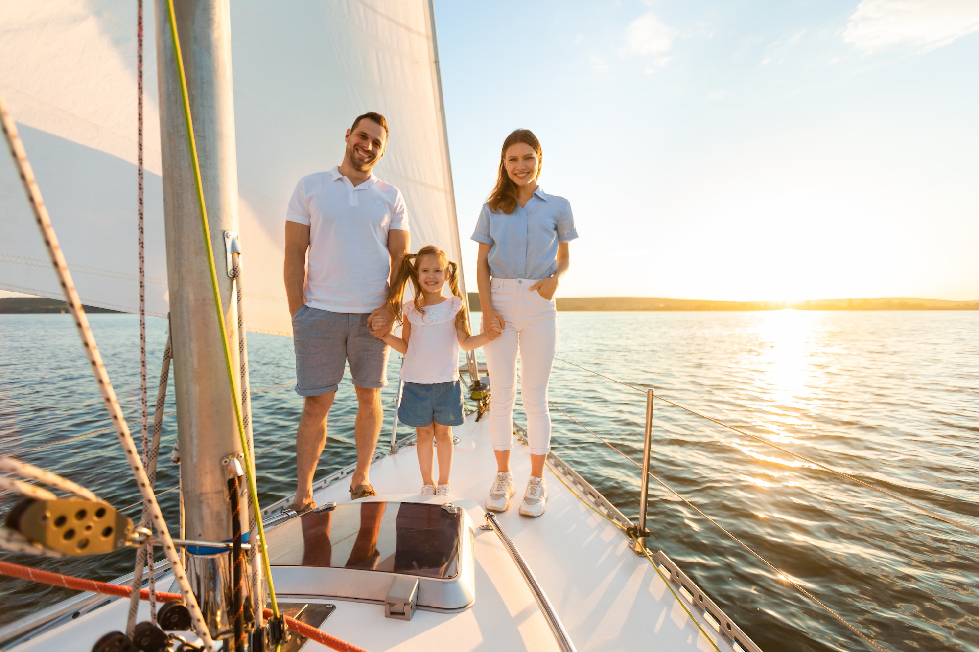 Family Standing On Boat Deck Sailing On Yacht In Sea