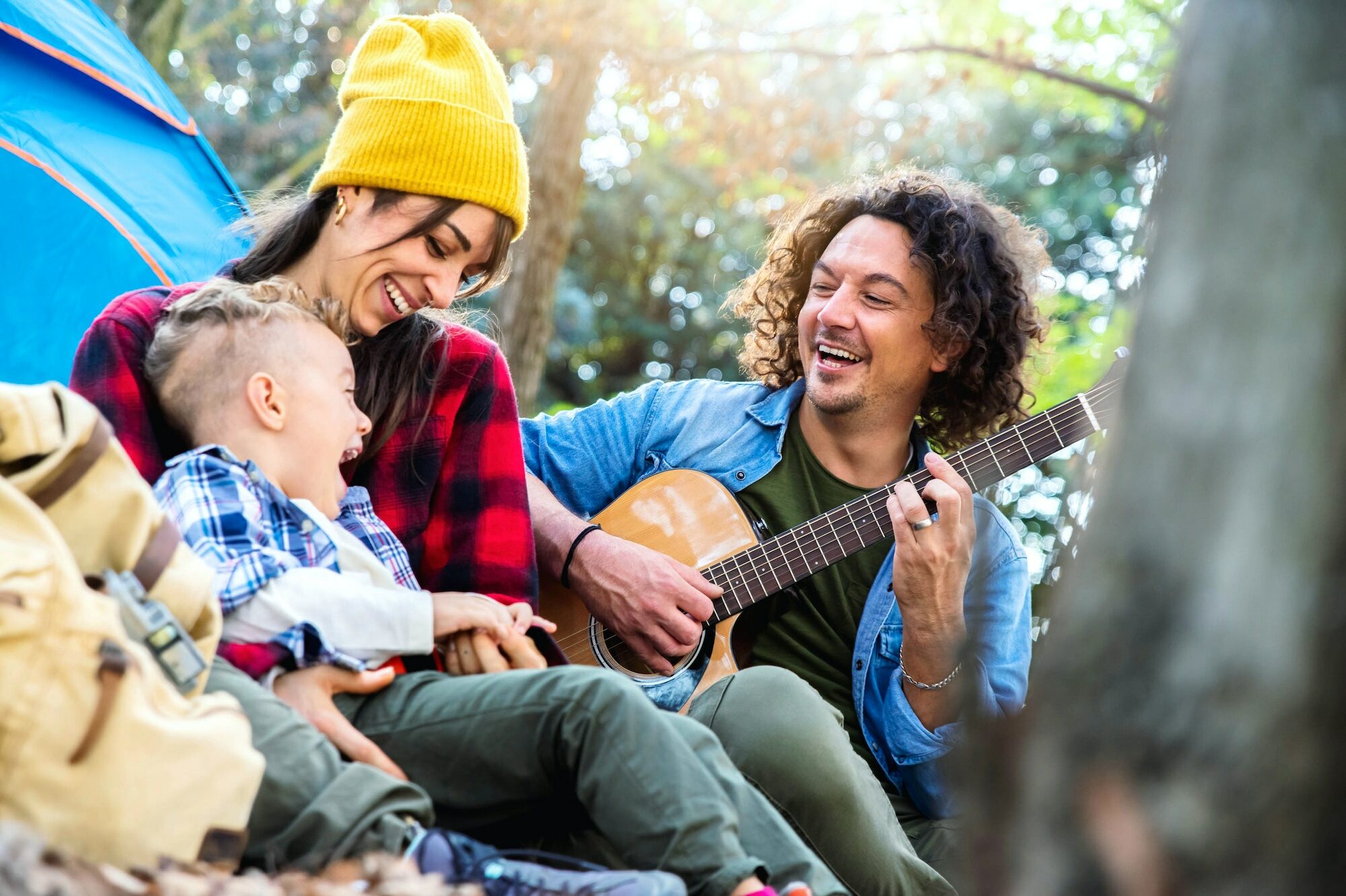Happy family camping in the forest playing guitar and singing together