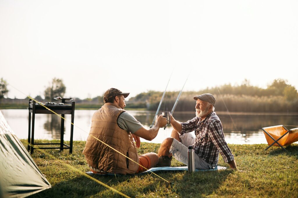 Happy father and son toasting while fishing and camping in nature.