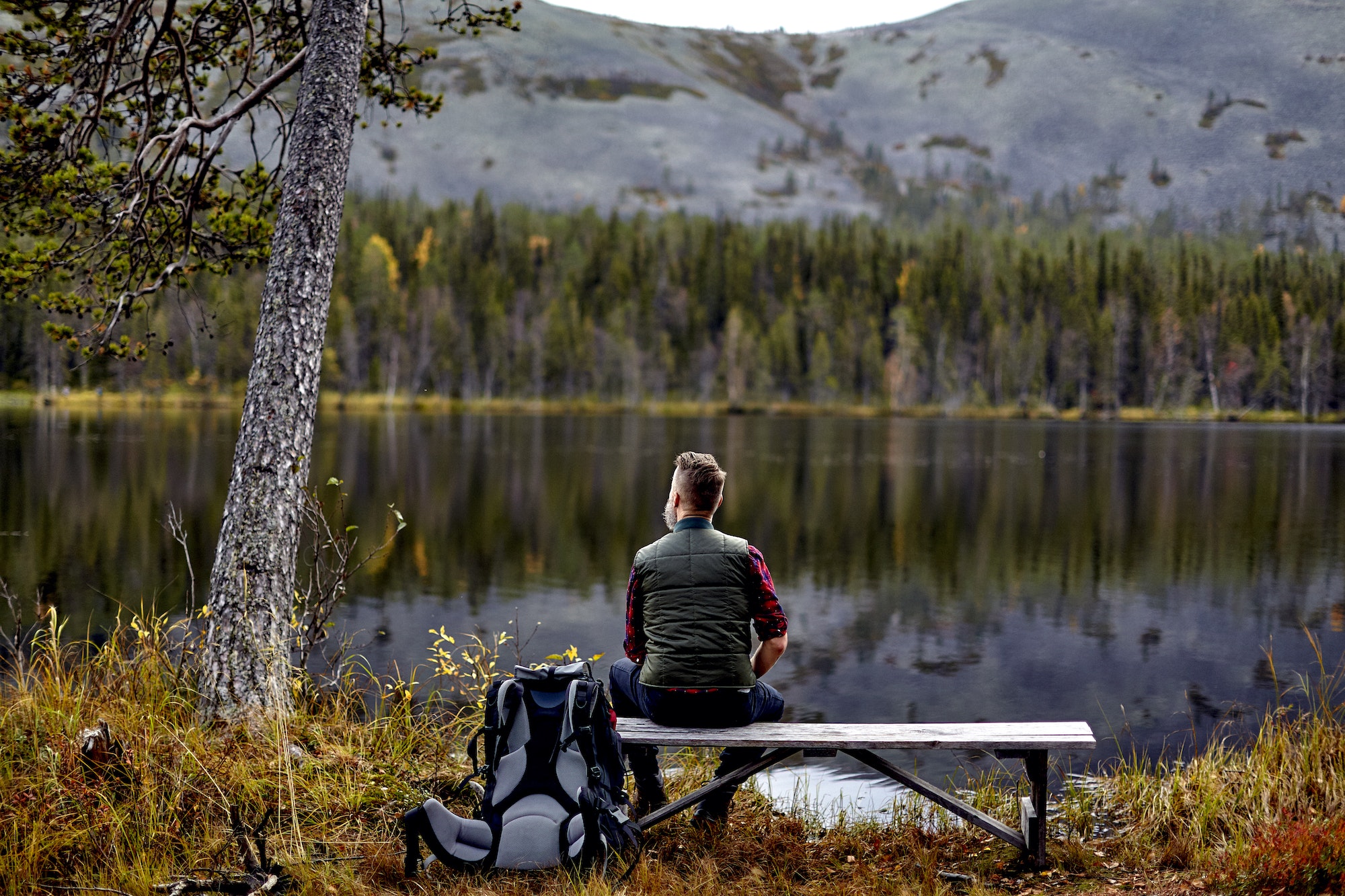 Hiker resting on bench, looking out at lake, Kesankijarvi, Lapland, Finland