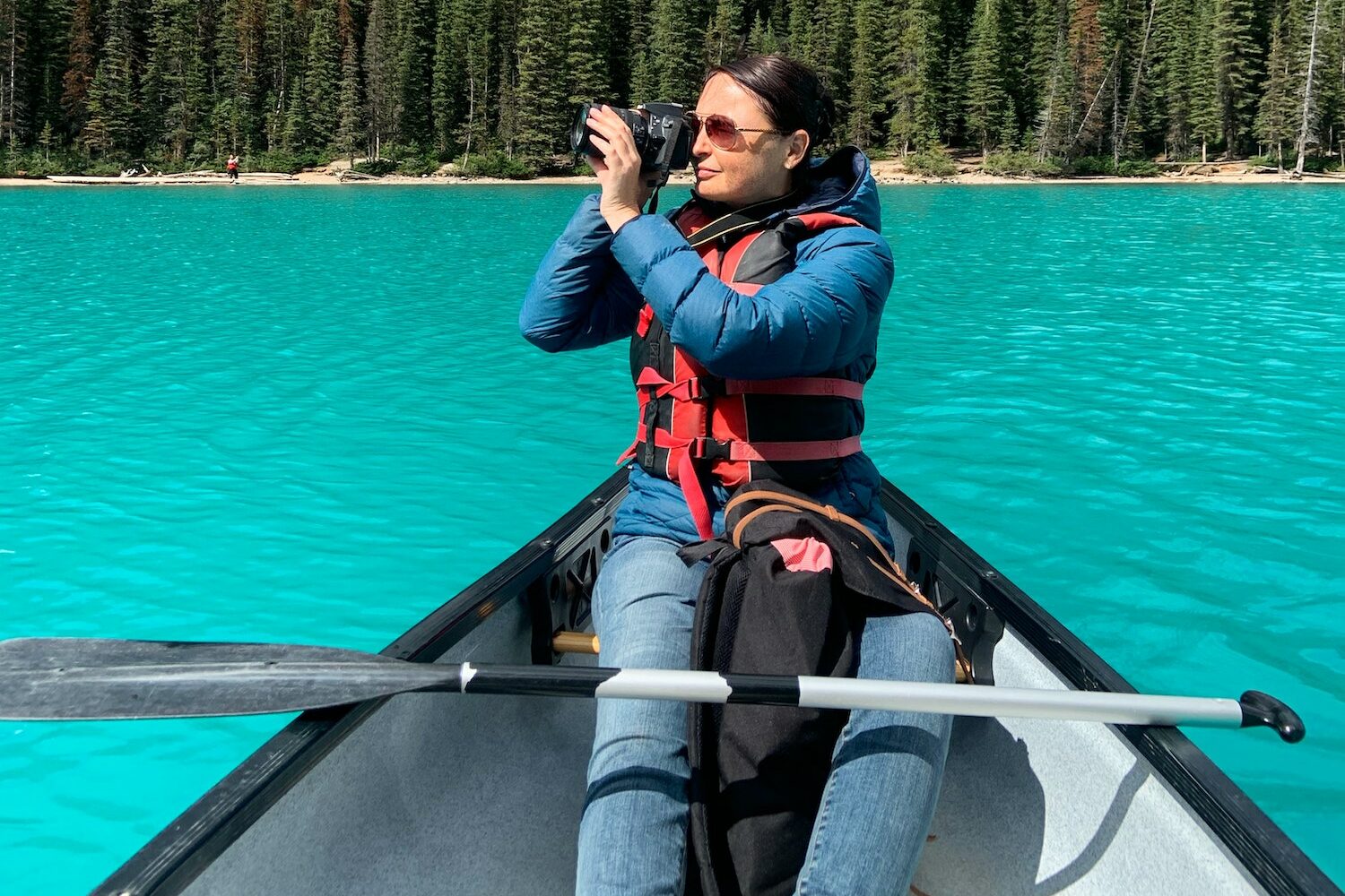 Middle aged woman in canoe on turquoise blue lake taking photos with digital camera
