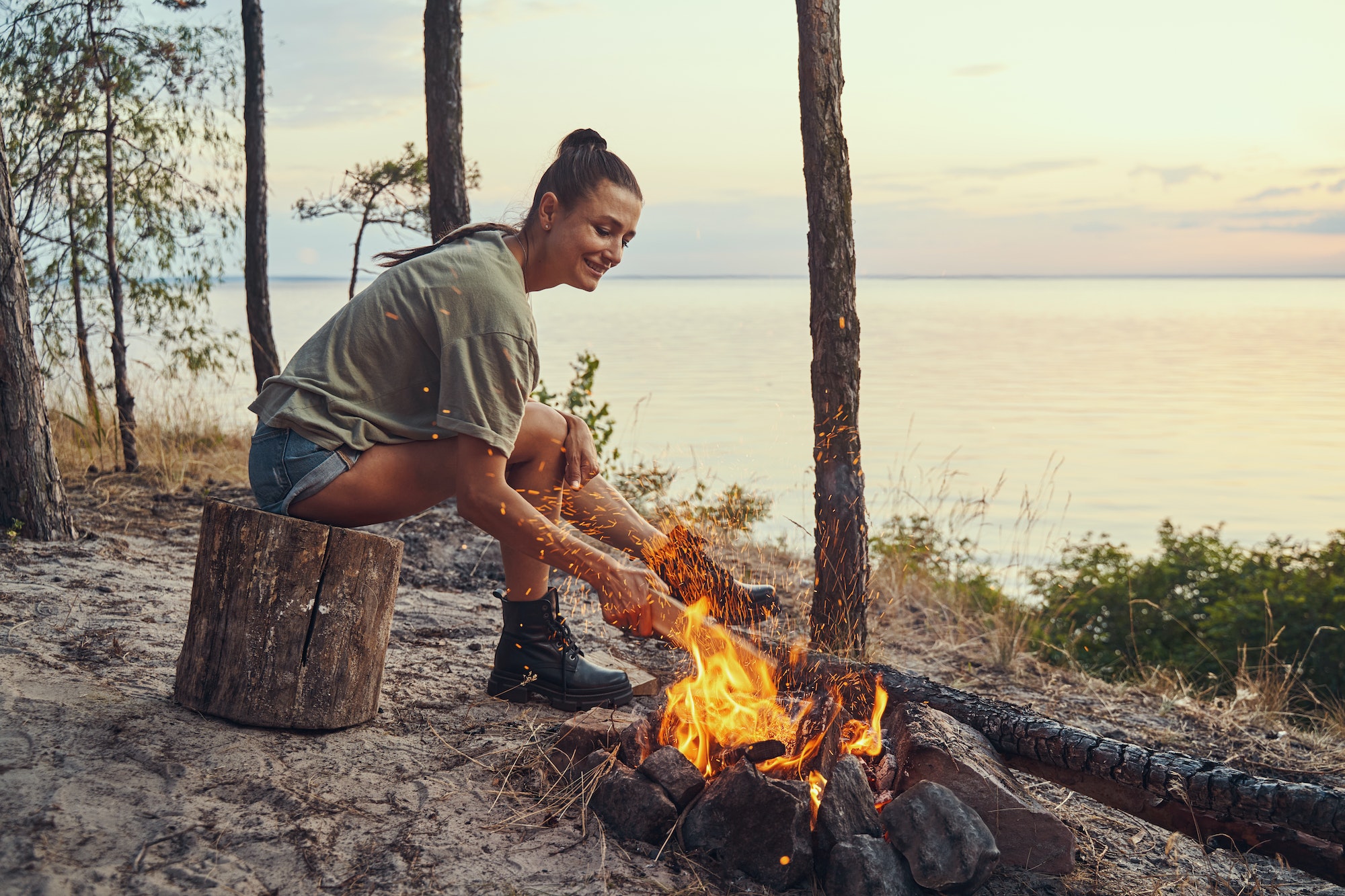 Pretty woman stirring burning logs in campfire