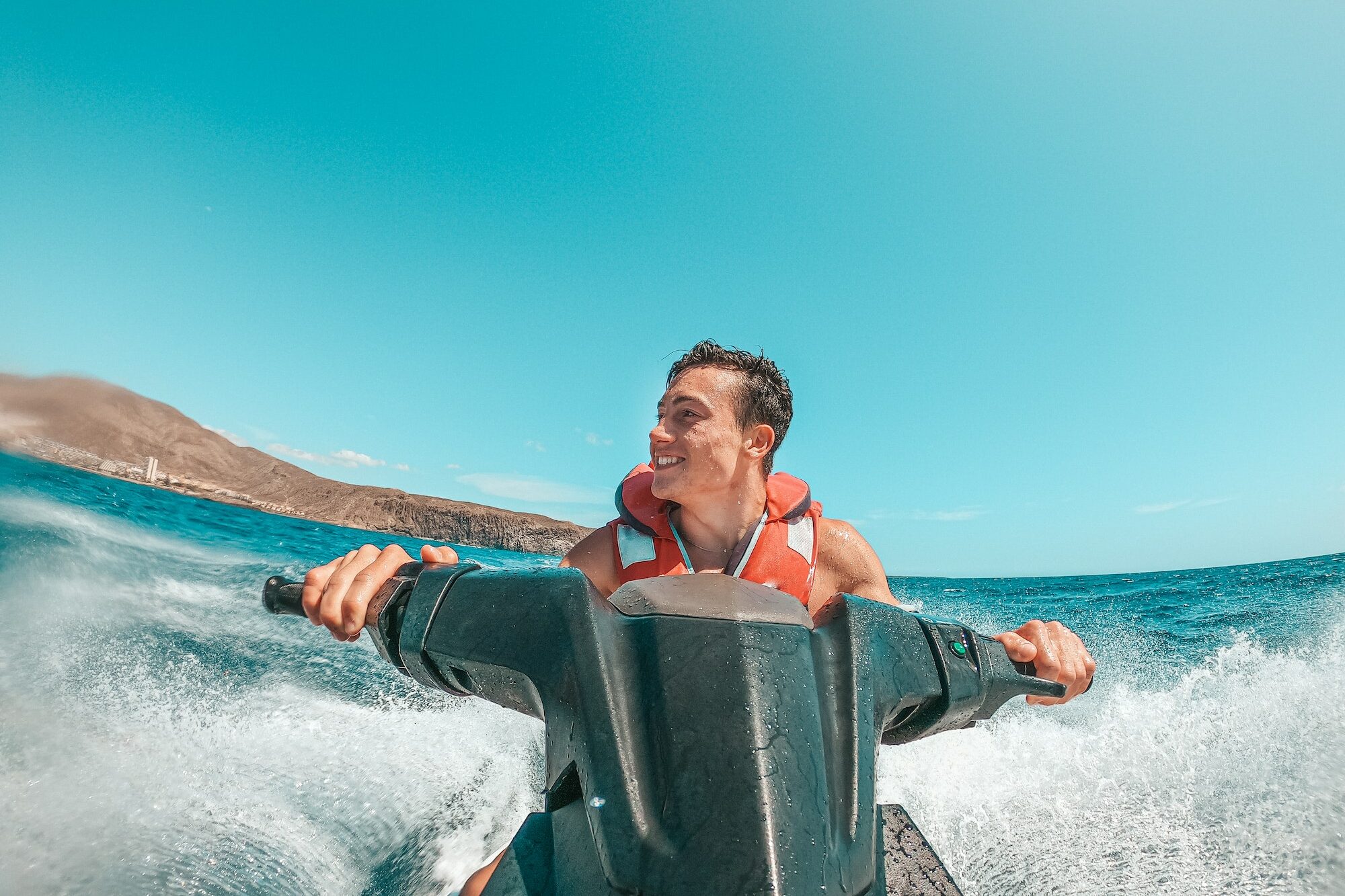 Teenager man enjoying summer in a jet ski in the middle of the sea having fun