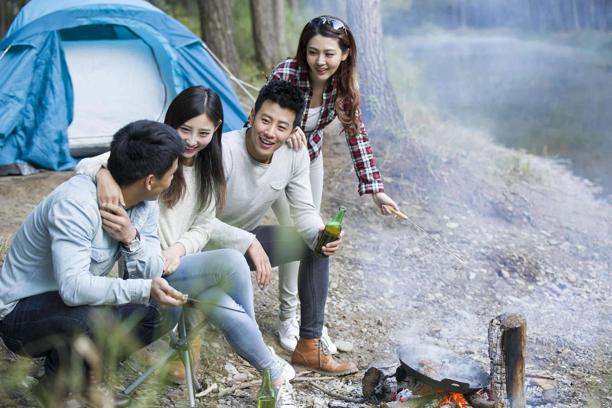 Young friends sitting beside campfire preparing food