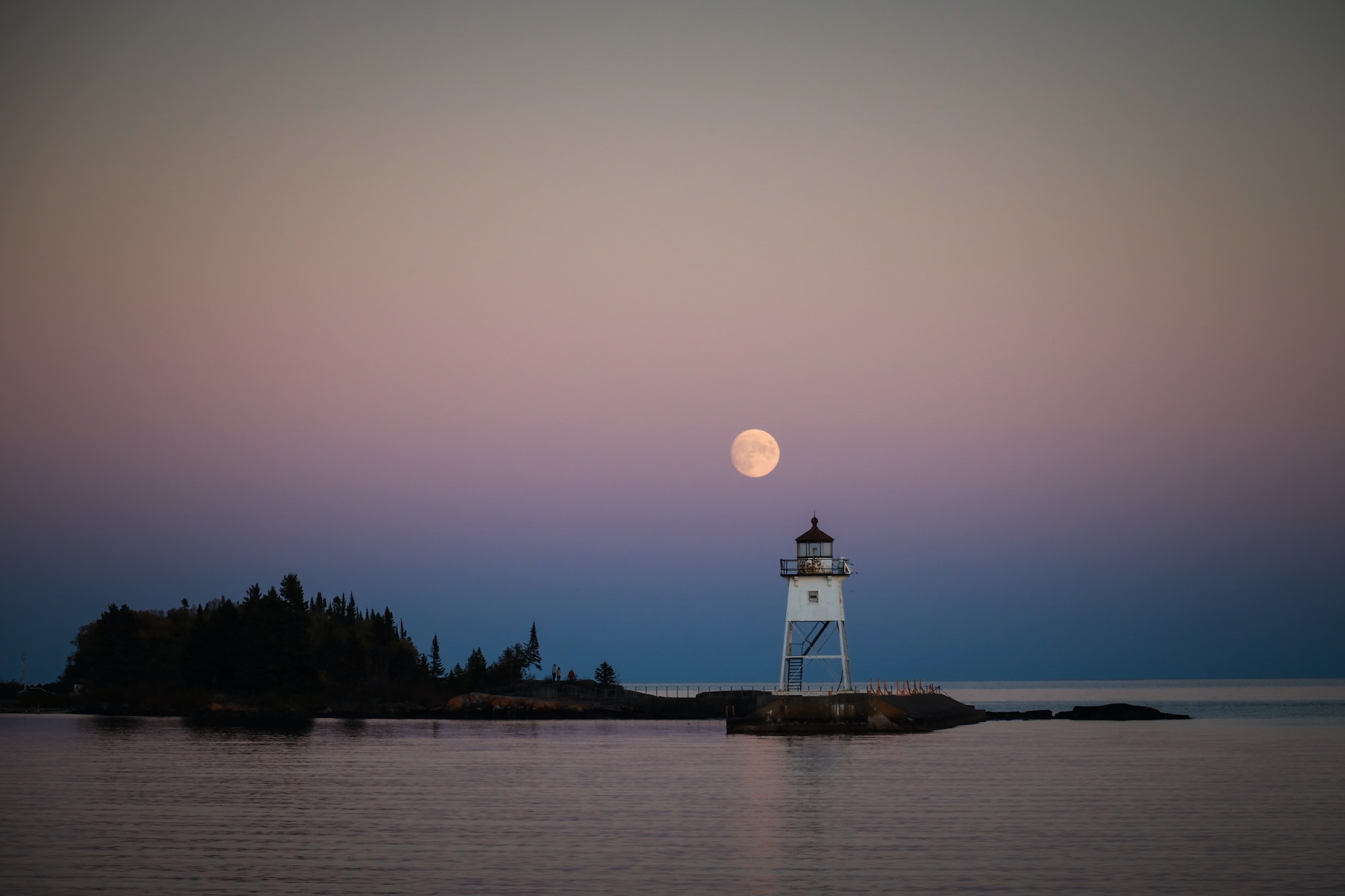 Full moon rising behind lighthouse over Lake Superior in Grand Marais, Minnesota.