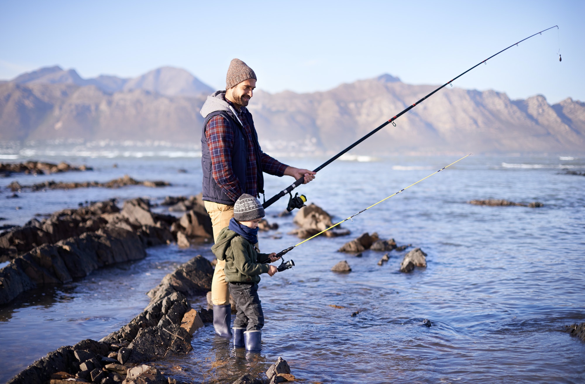 Looks like we have company. Shot of a cute little boy fishing with his father by the sea.