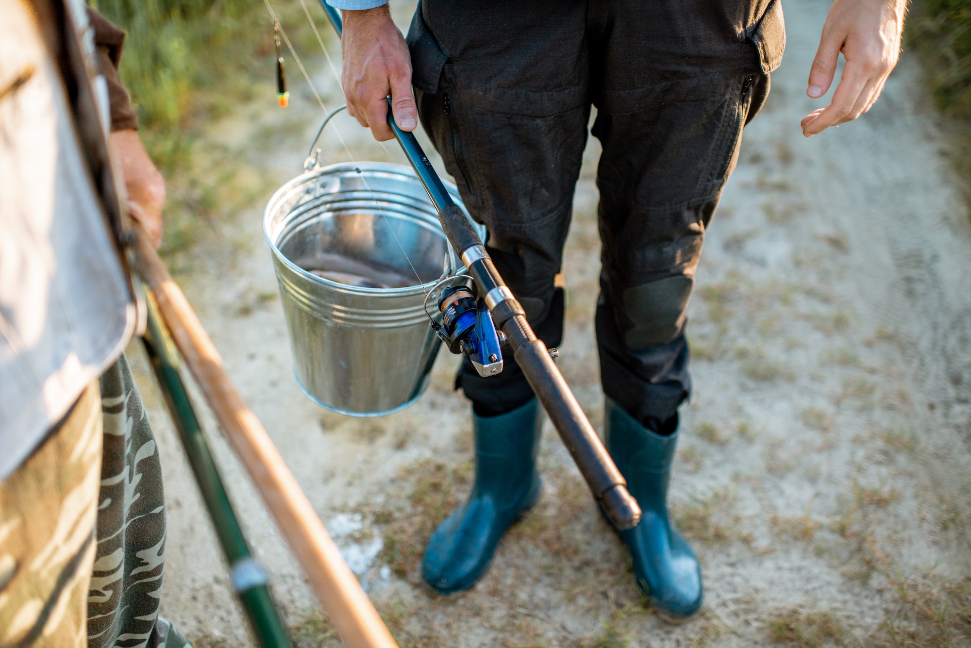 Holding fishing rods and bucket with fish outdoors