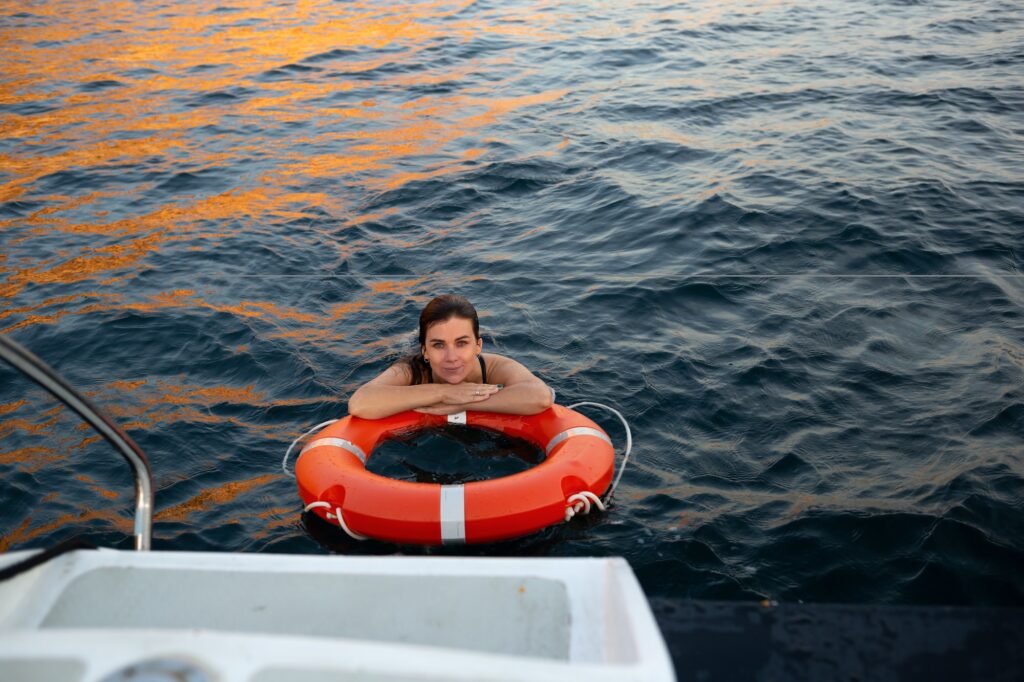 young woman resting on a lifebuoy in the sea near the yacht